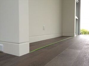 White baseboards installed along the edge of light wood laminate flooring in a modern interior, creating a clean and seamless transition between wall and floor.